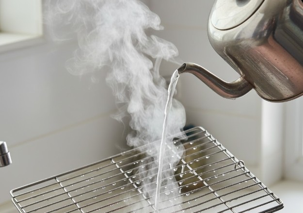 徹底的な殺菌消毒のため、ピカピカに磨かれたステンレス製の鳥かごの網に、湯気の立つ熱湯をかけている様子。衛生管理を重視する飼い主の経験を表現。